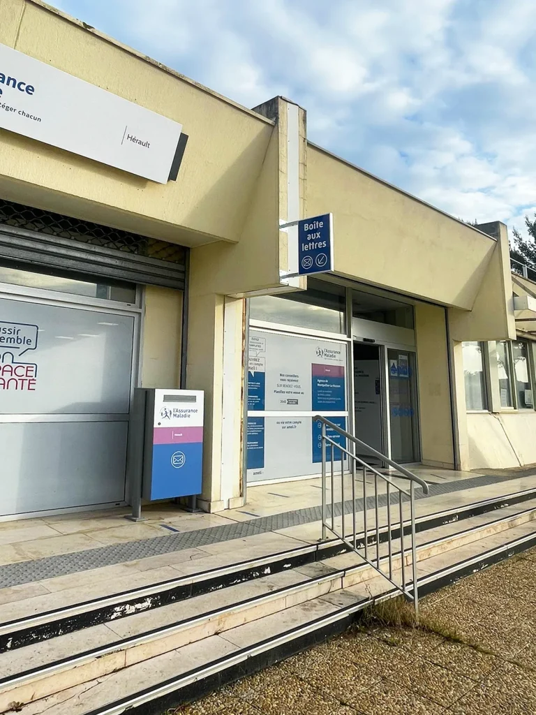 Enseigne à Montpellier : enseigne drapeau bleue « Boîte aux lettres » fixée en façade de la CPAM, à l’entrée du site