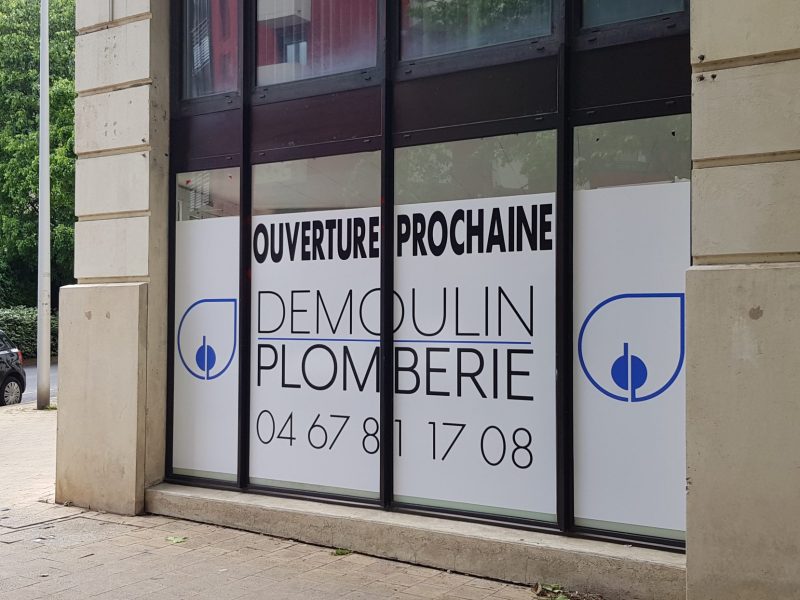 Vitrine habillée d'un adhésif blanc annonçant l'ouverture prochaine de Demoulin Plomberie