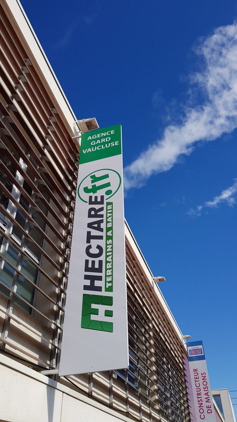 Enseigne bandeau blanche et verte en façade avec projecteur, agence Hectare