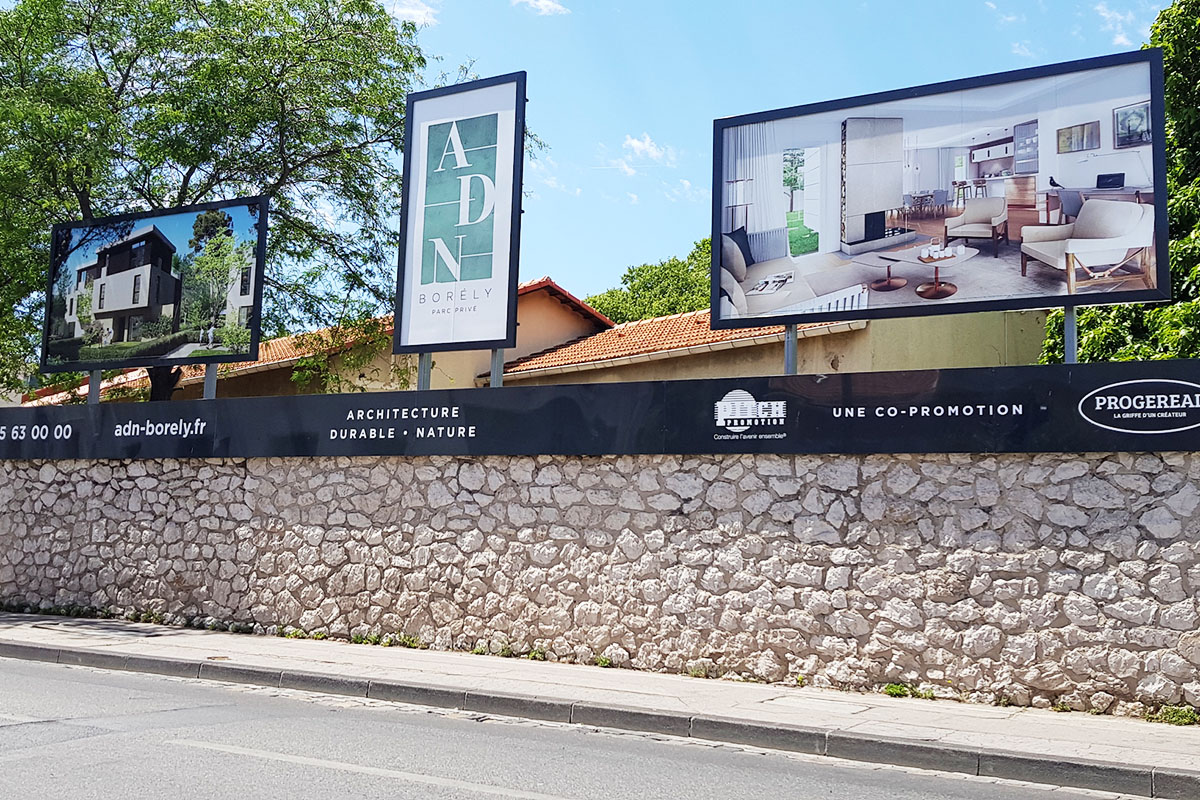Panneaux publicitaires immobiliers sur mesure installés au-dessus d’un mur en pierre